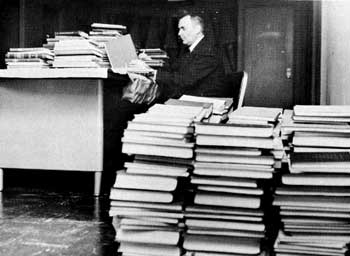 Man working at a desk with piles of books around his chair