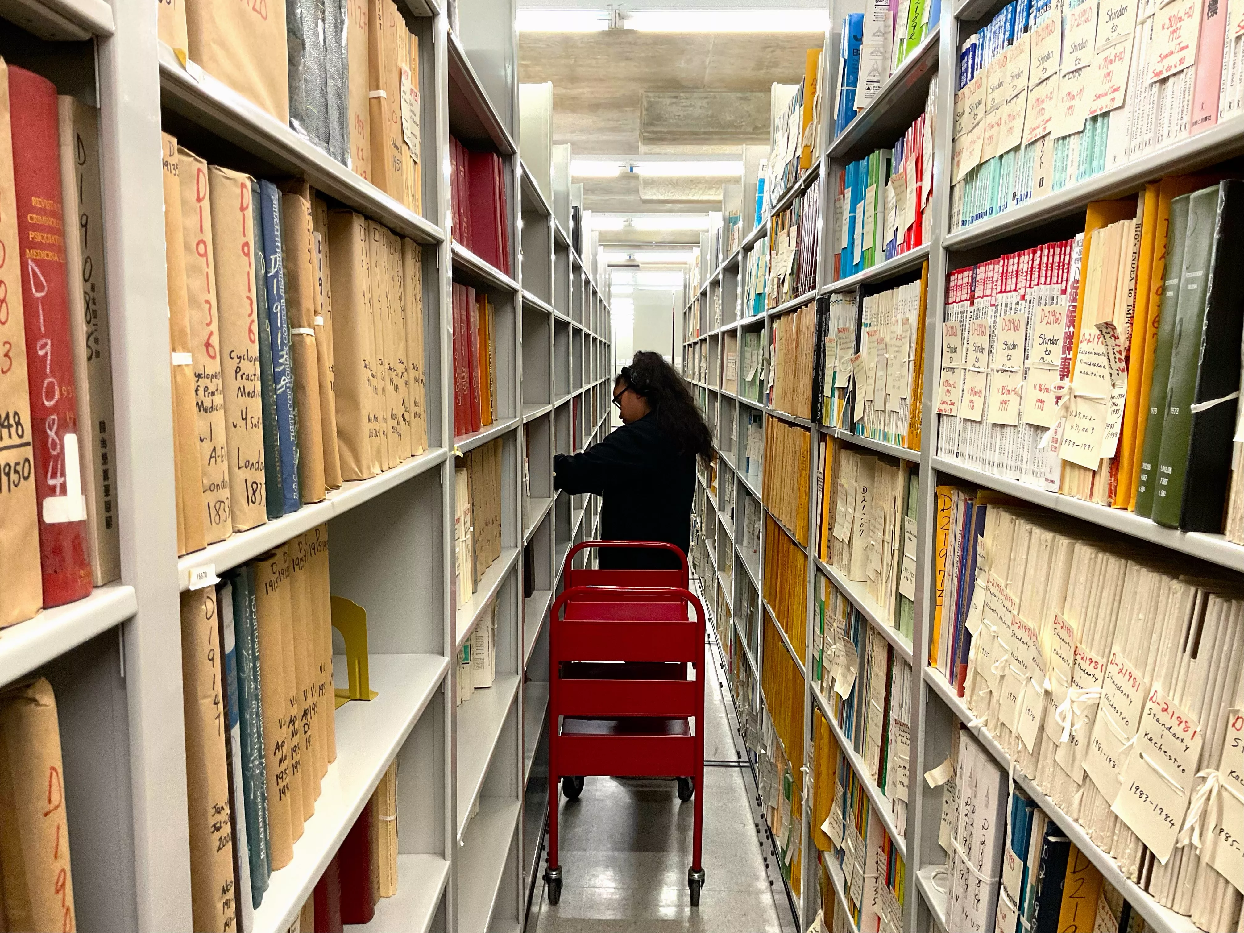 A CRL employee looks through our stacks with a cart filled with materials beside them.